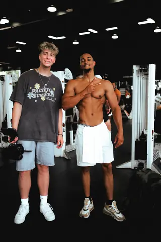 Malakai with a camera on the gym floor next to a fitness creator after a shoot