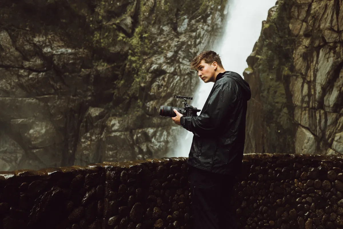 Malakai filming beside a huge waterfall in a misty canyon
