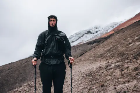 Malakai in a rain jacket on a mountain slope with trekking poles