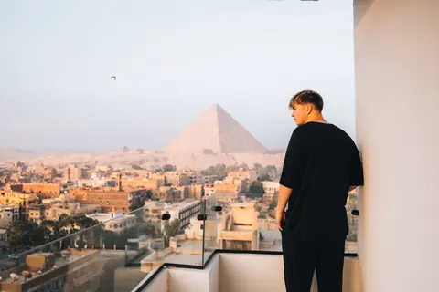 Malakai on a balcony with the Great Pyramid rising behind the city