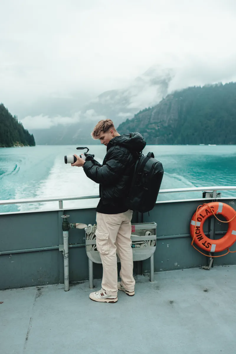 Malakai filming from the deck of a ferry, misty mountains across the water