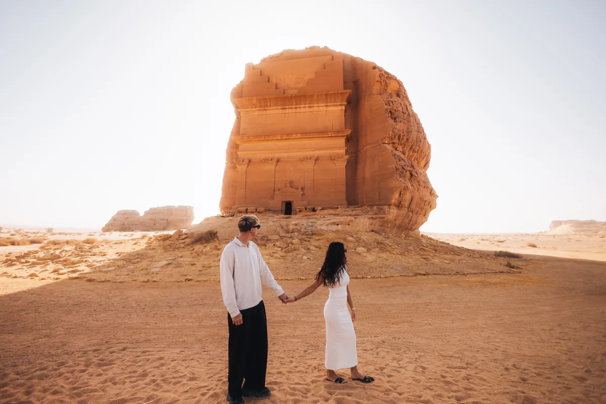 Malakai and Maddie holding hands in the desert in front of a carved rock tomb