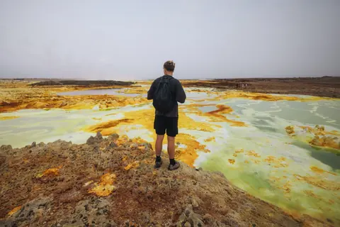Malakai standing among yellow-green geothermal pools at Dallol