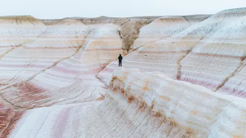 Malakai alone on a ridge of pink and white striped hills