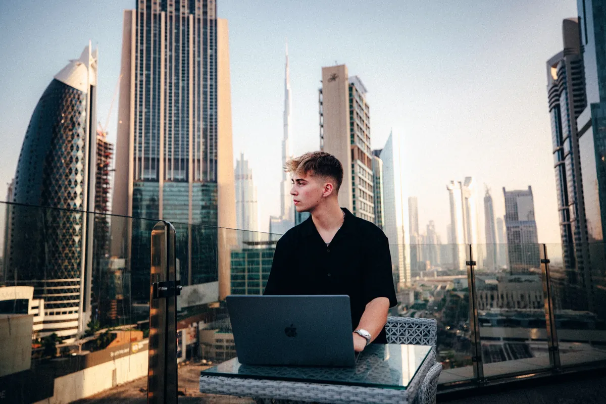 Malakai working on a laptop on a terrace, a skyline behind him