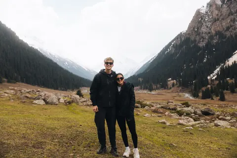 Malakai and Maddie together in an alpine valley under snowy peaks