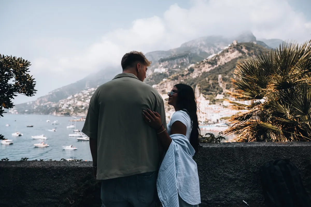 Malakai and Maddie holding each other above the sea, a cliffside town behind them