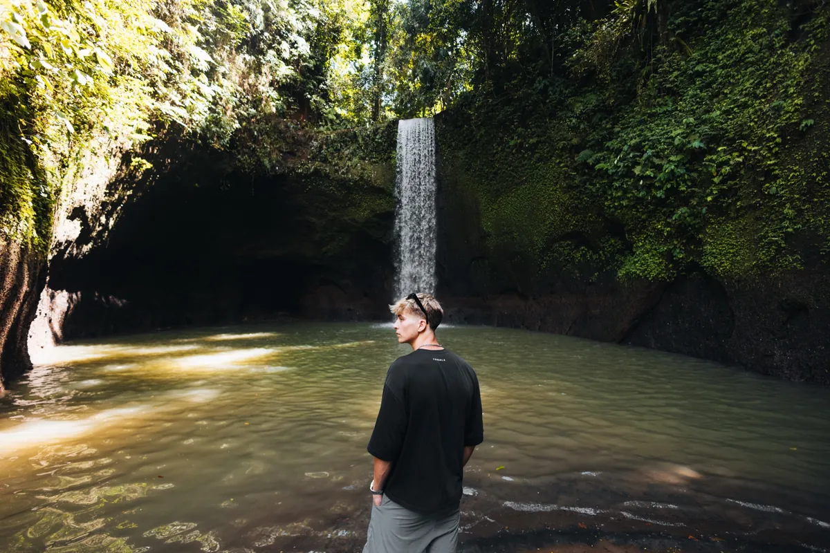 Malakai standing in the pool in front of a jungle waterfall