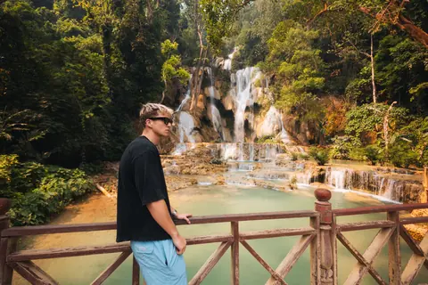 Malakai on a wooden bridge in front of turquoise waterfall pools