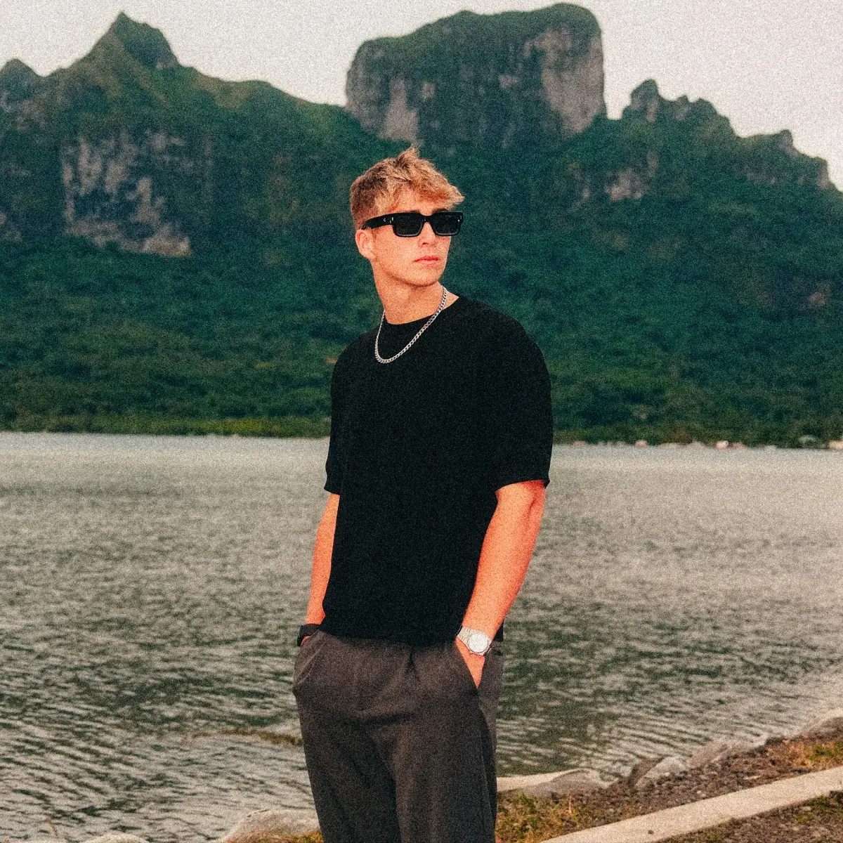 Malakai in sunglasses by a lagoon, green mountains behind him