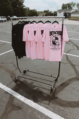 A rack of pink and black Detached Apparel t-shirts in a parking lot