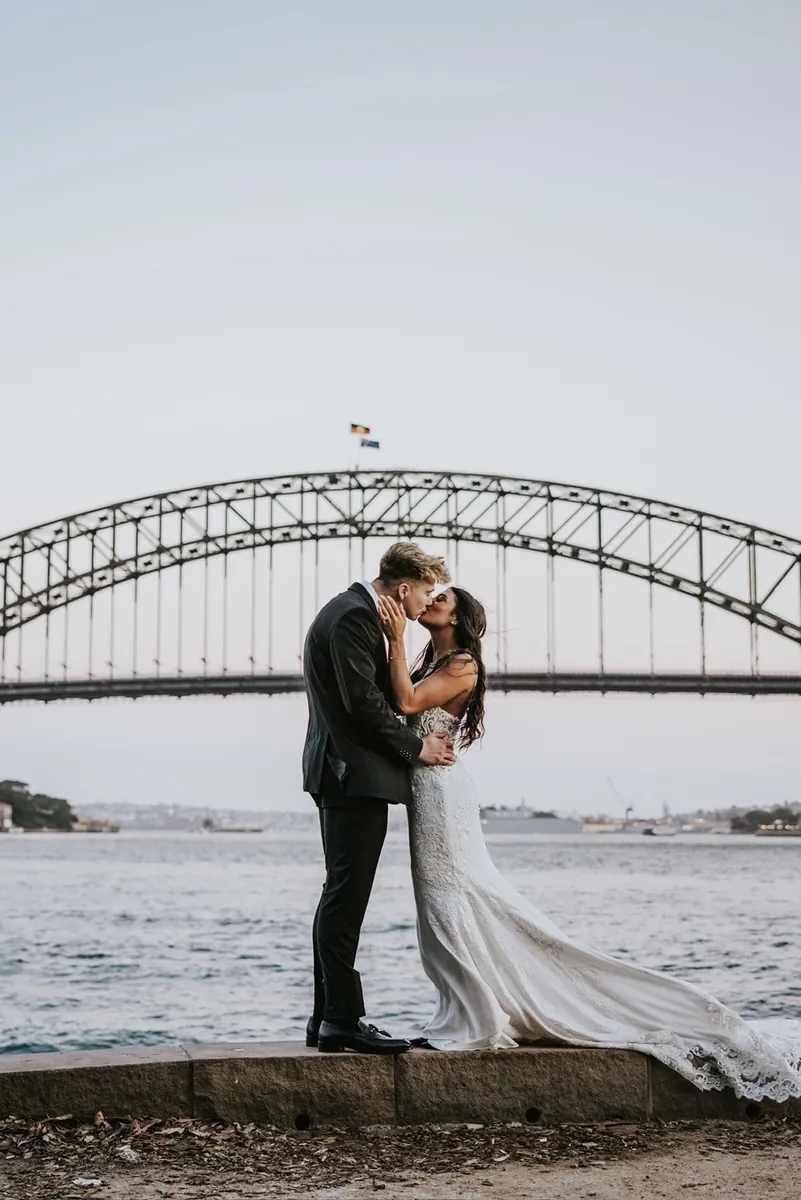 Malakai and Maddie kissing on the harbour wall in her wedding dress, the Sydney Harbour Bridge behind them