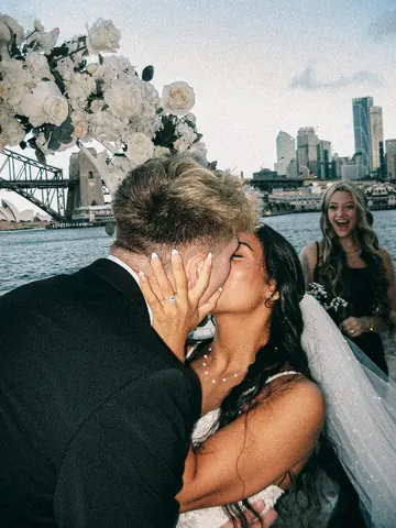 A close kiss with the city skyline and a smiling guest behind them